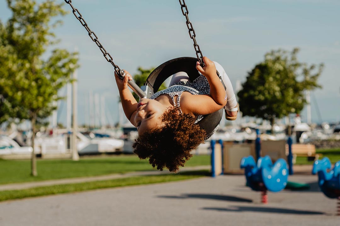young girl swinging, looking back upside-down 
