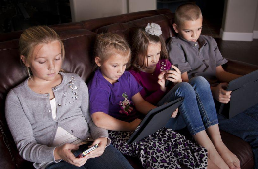 Children on couch playing with digital devices