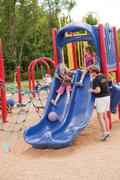 Girls sliding down slide with adult observing