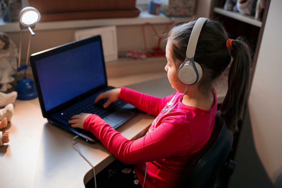 Little girl listening to music while studying on the computer