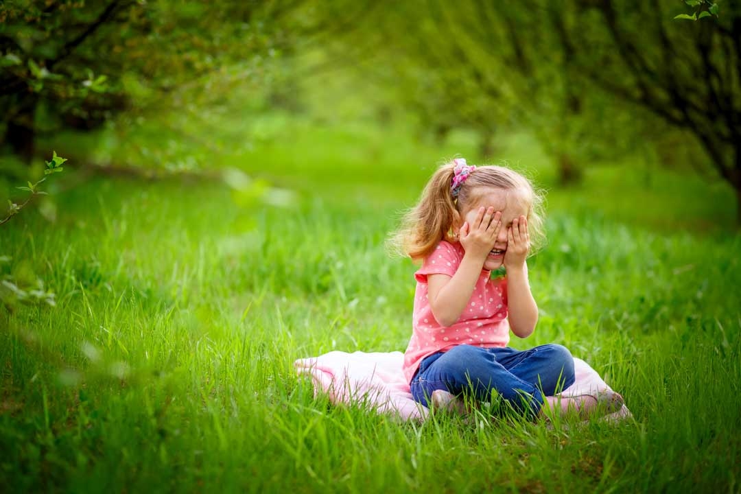 Young girl playing hid in seek in green grass