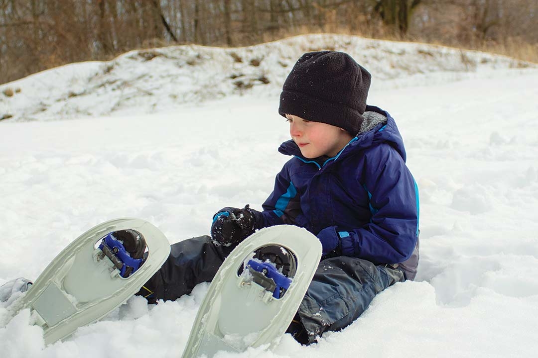 boy in snowshoes sitting in snow