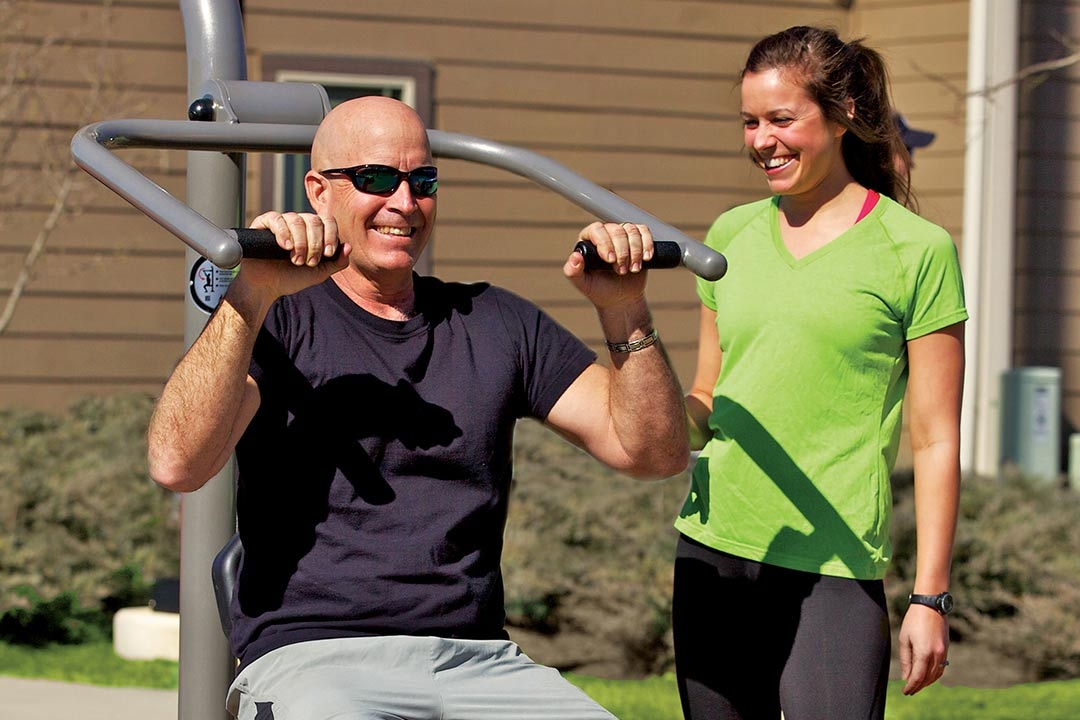Couple doing shoulder presses on park fitness equipment