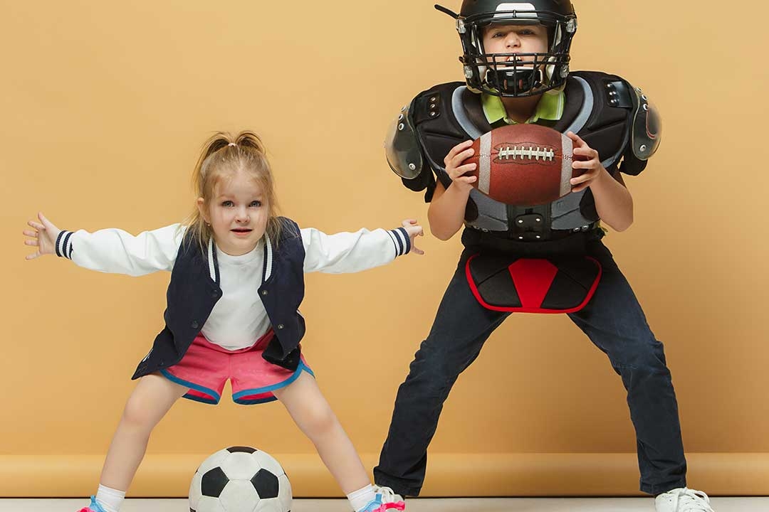 two children, one with soccer ball, one with football/football gear.