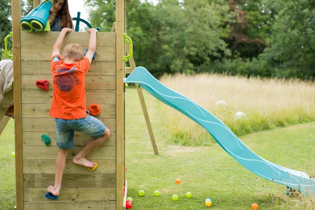 Child climbing a wooden rock wall on a Plum Play backyard playset with teal slide available from The Best Backyard Australia