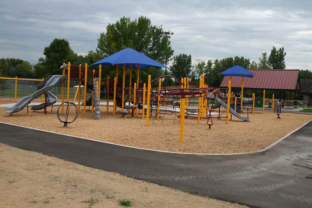 Commercial playground equipment installed by St. Croix Recreation at a Minnesota community park, featuring slides, climbing structures, and blue shade canopies over wood chip surfacing