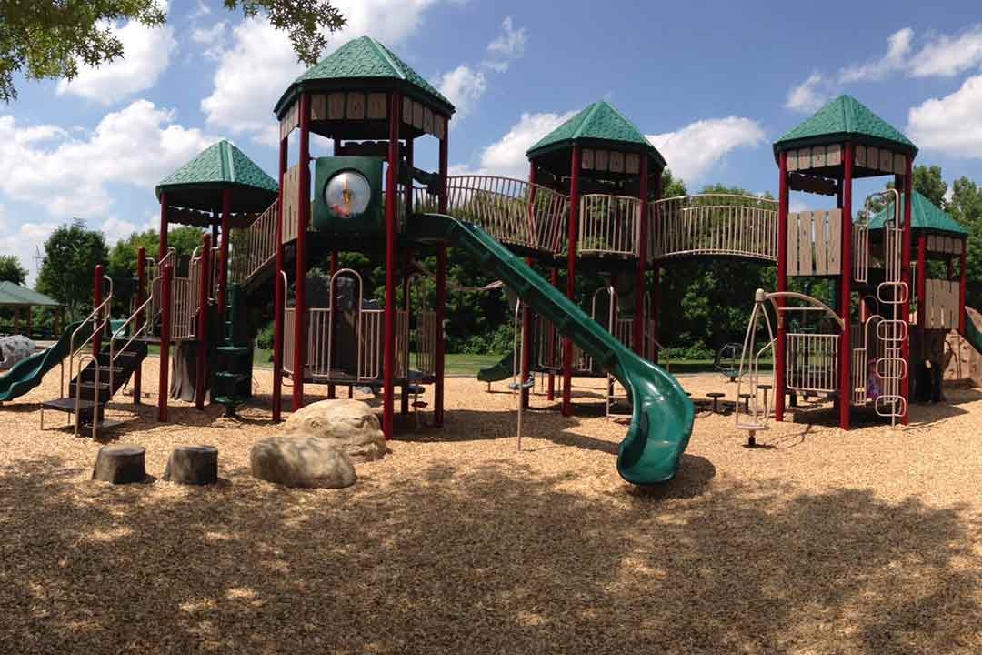 Large commercial playground structure with green castle-style towers, tube slide, and wood chip surfacing installed by St. Croix Recreation at a Minnesota park
