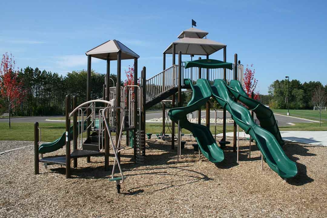 BCI Burke commercial playground equipment with multi-lane green slides and shade canopies installed by St. Croix Recreation at a Minnesota community park in fall