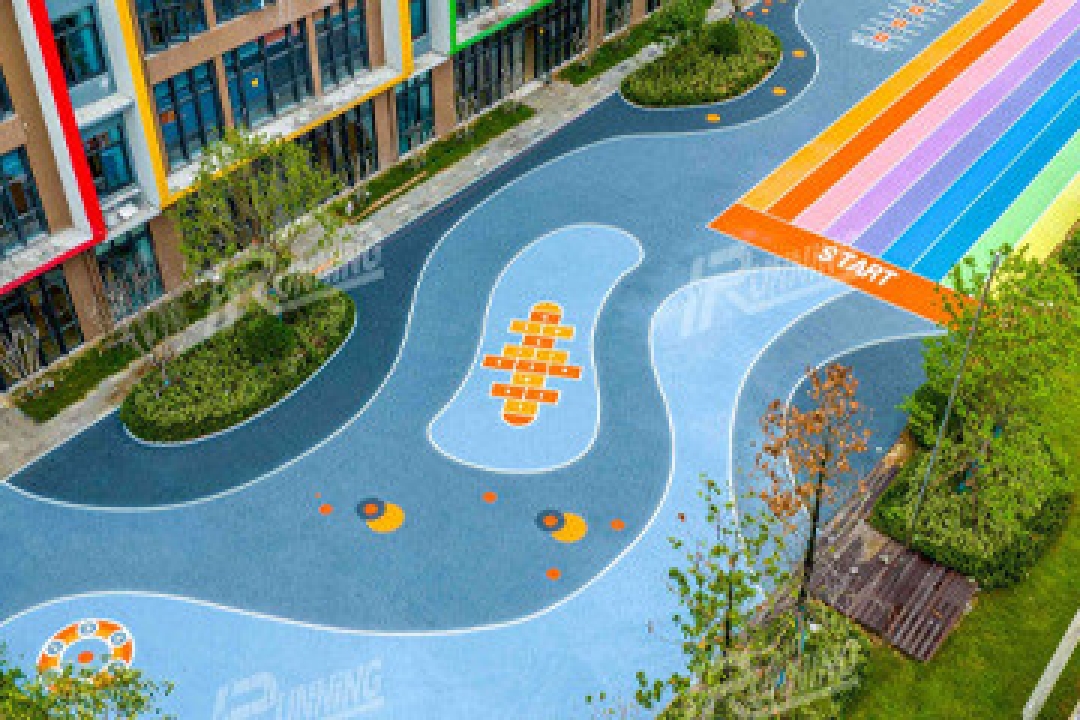  A colorful aerial view of a children's playground area featuring a winding blue rubber track with bright orange and yellow designs, a rainbow-striped section, …A colorful aerial view of a children's playground area featuring a winding blue rubber track with bright orange and yellow designs, a rainbow-striped section, and surrounding greenery next to a modern building.