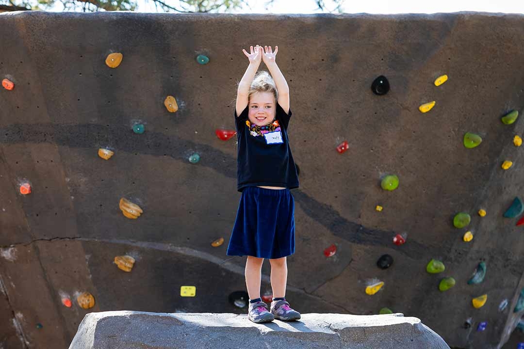 Young girl standing triumphantly on an EP Climbing Freeform outdoor boulder at Alpenglow Community Park in Bend Oregon