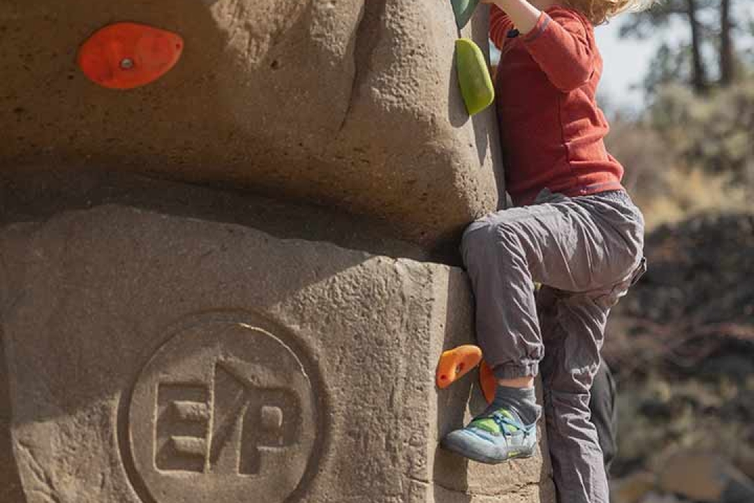 Child scaling an EP Climbing branded outdoor park boulder with colorful holds at Alpenglow Community Park Bend Oregon
