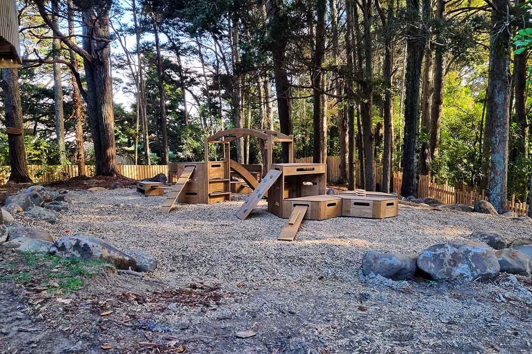 Outdorable modular timber play equipment set in a natural woodland setting with engineered wood fiber surfacing and boulder borders