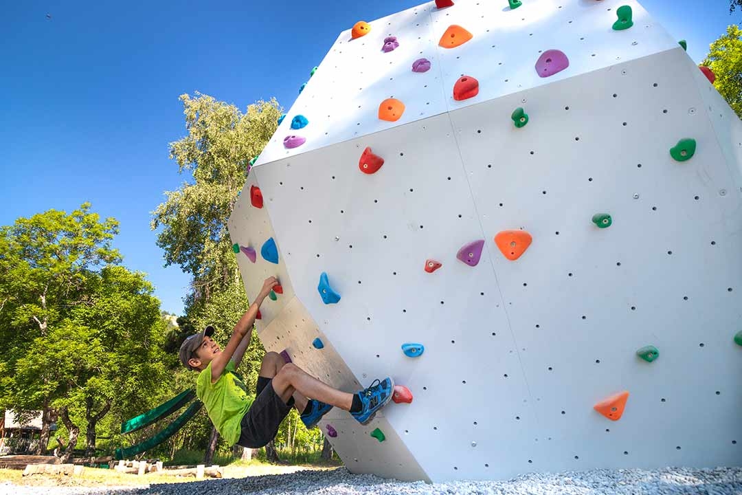Child bouldering on an EP Climbing MozaiK XP outdoor modular climbing wall with colorful holds in a park setting