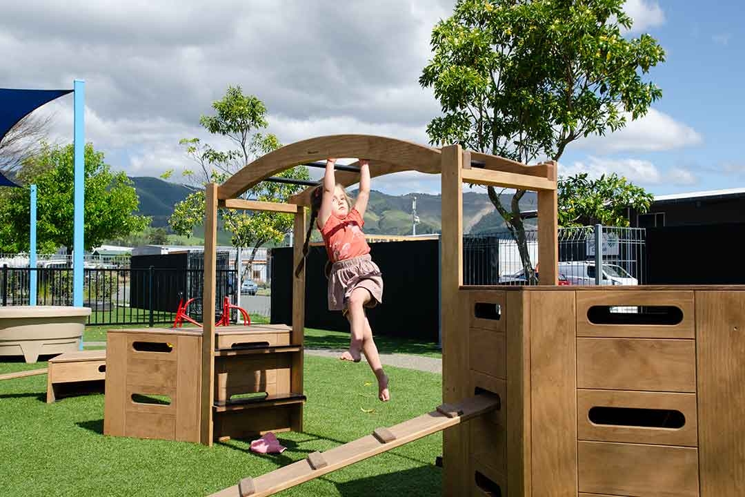Child hanging from Outdorable timber arch climbing frame developing upper body strength and gross motor skills outdoors