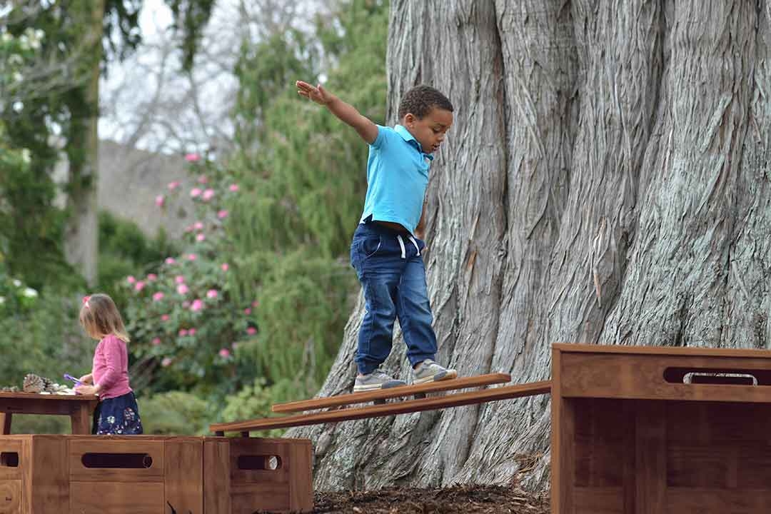 Child balancing on an Outdorable timber ramp between modular play blocks promoting balance and coordination in an outdoor park setting