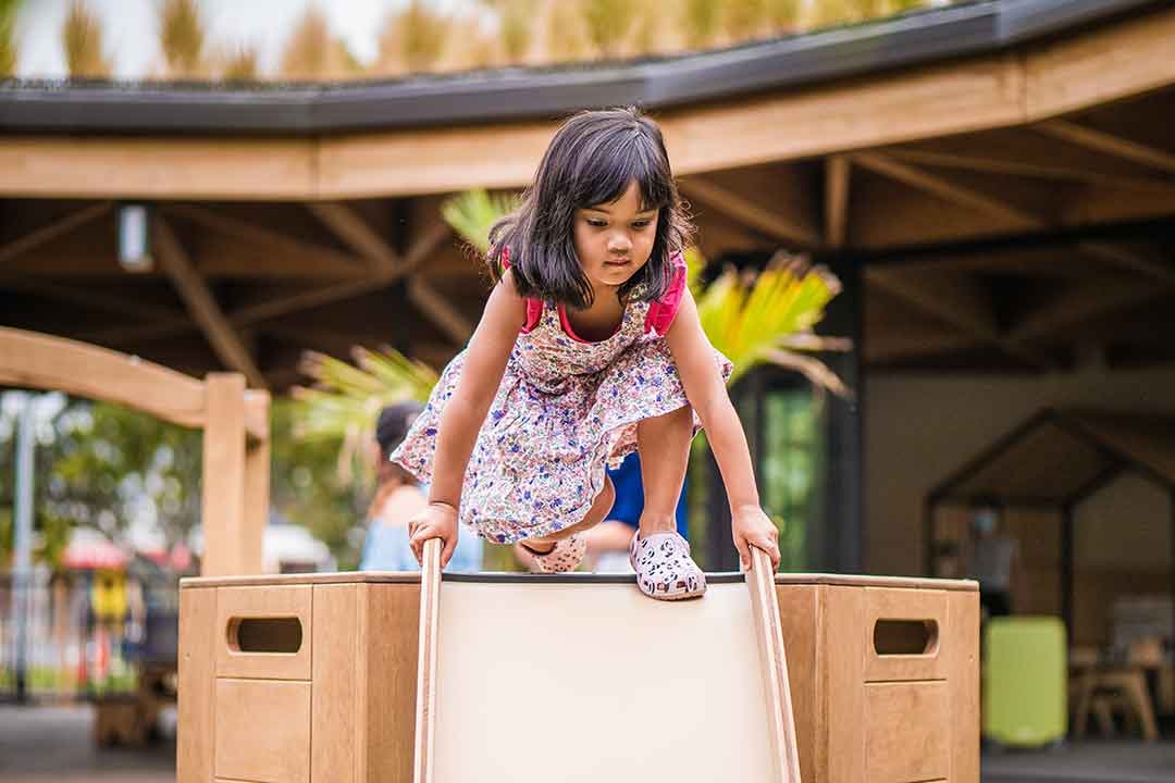 Young girl climbing over an Outdorable timber play module developing physical confidence and problem-solving through open-ended play