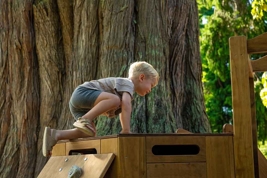 Toddler climbing an Outdorable natural timber play block developing physical confidence and gross motor skills in an outdoor garden setting