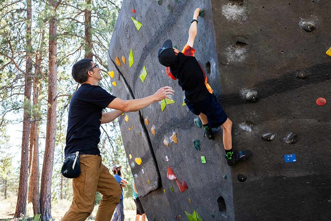 Adult spotting a child bouldering on an EP Climbing outdoor park boulder wall demonstrating accessible community climbing for all ages