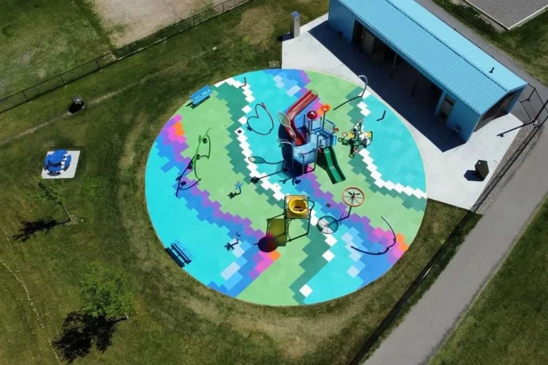  A stunning aerial view of a circular playground featuring Life Floor's vibrant multi-colored geometric safety surfacing with custom inlay designs, surrounding …A stunning aerial view of a circular playground featuring Life Floor's vibrant multi-colored geometric safety surfacing with custom inlay designs, surrounding a colorful play structure in the center of a grassy park.