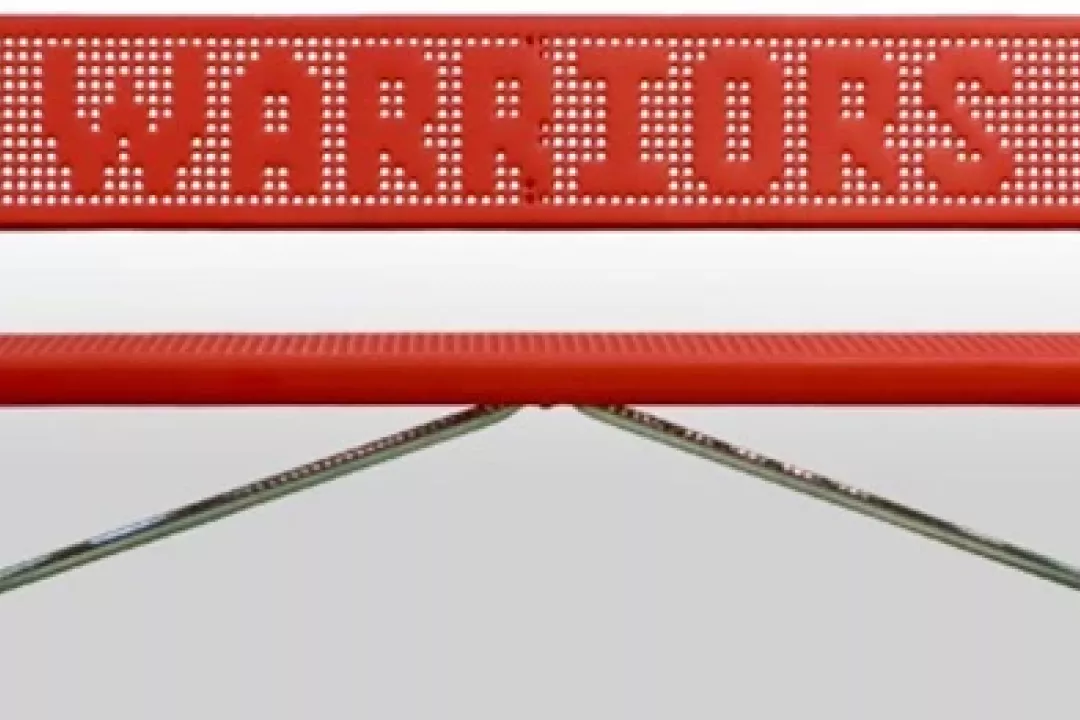  A bold red perforated steel "Warriors" team bench with galvanized metal legs, ideal for athletic sidelines.