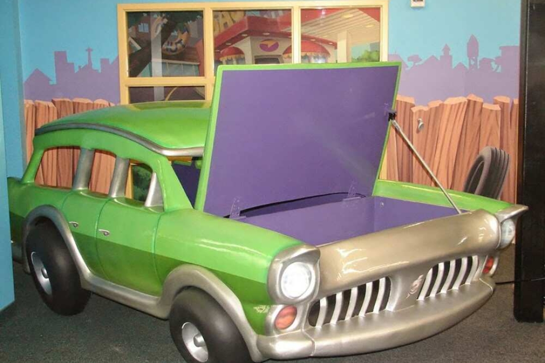 A fun, cartoonish green sculpted car with an opening hood serves as an interactive play feature inside a themed children's space.