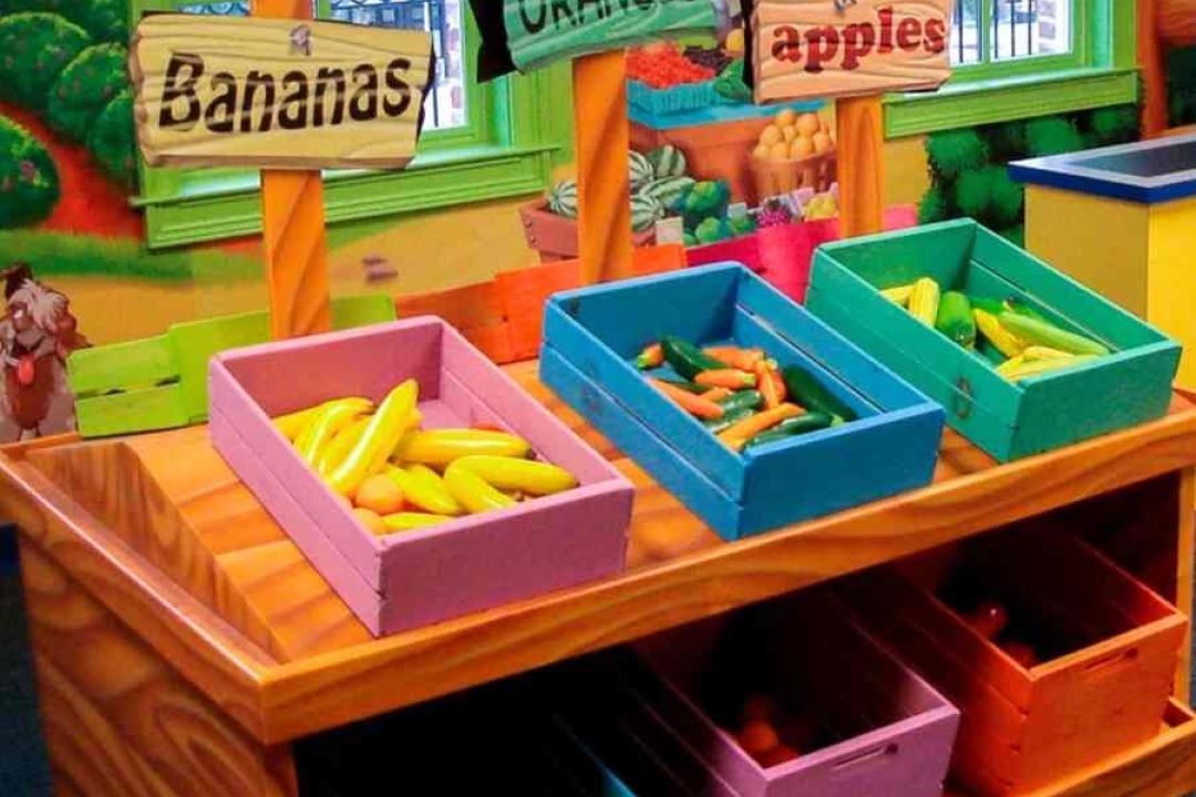 A colorful themed farmer's market play station with labeled wooden crates of toy fruits and vegetables brings a charming interactive element to a children's space.