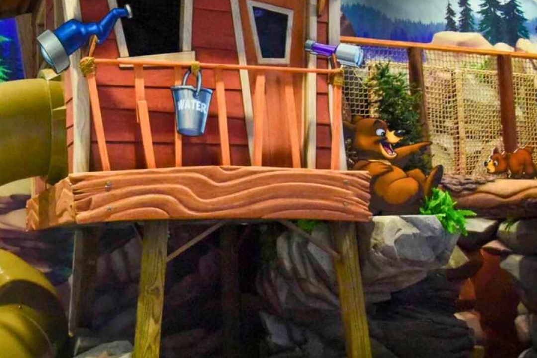 A detailed sculpted treehouse with a slide, rope netting, and a mountain camping mural creates an adventurous indoor play environment.