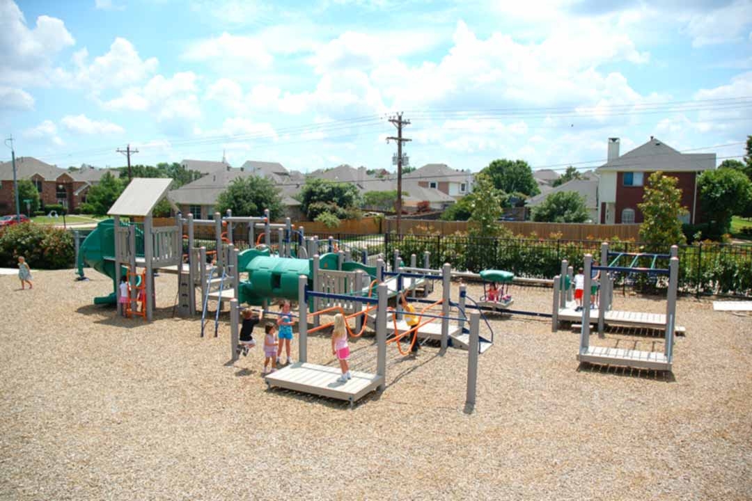 Children playing on a multi-structure community playground with engineered wood fiber surfacing demonstrating proper use zone spacing between equipment