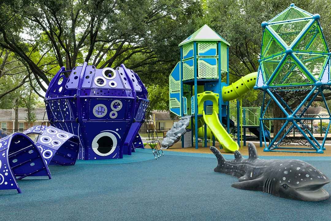 GameTime aquatic-themed playground at Carol Fox Park featuring the kraken climber whale shark play element and net climber under oak trees in Jersey Village Texas