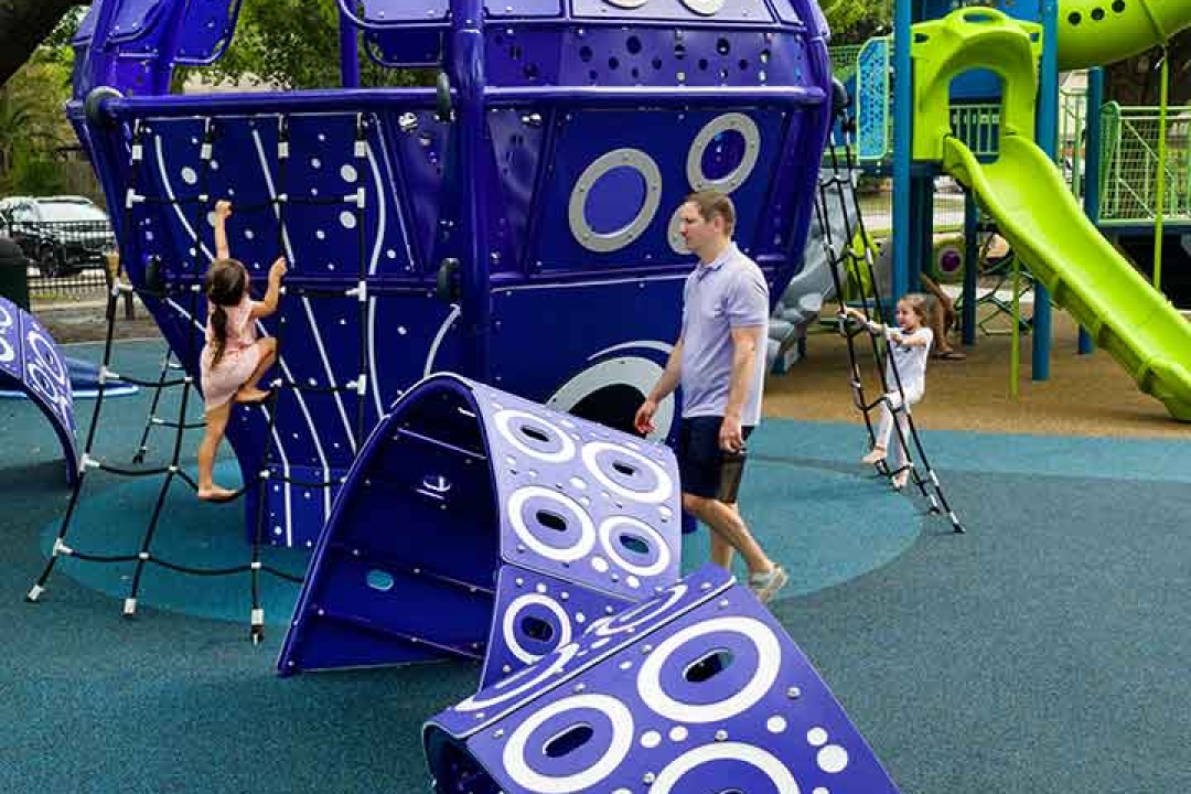 Father supervising children playing on the GameTime kraken climber and net structure at Carol Fox Park in Jersey Village Texas