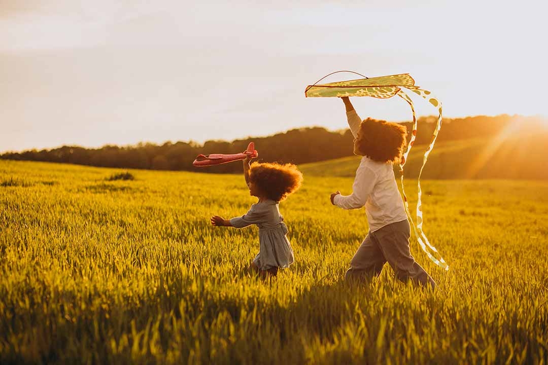 Children running and playing outdoors with a kite at sunset representing the joy and freedom of outdoor play over screen time