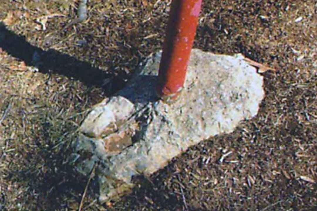 Red playground equipment post improperly anchored on top of a flat rock instead of being secured in the ground
