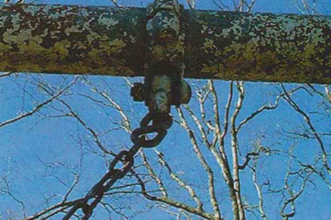 Upward view of a swing set crossbeam with severely peeling paint and a chain attachment showing significant weathering against a blue sky