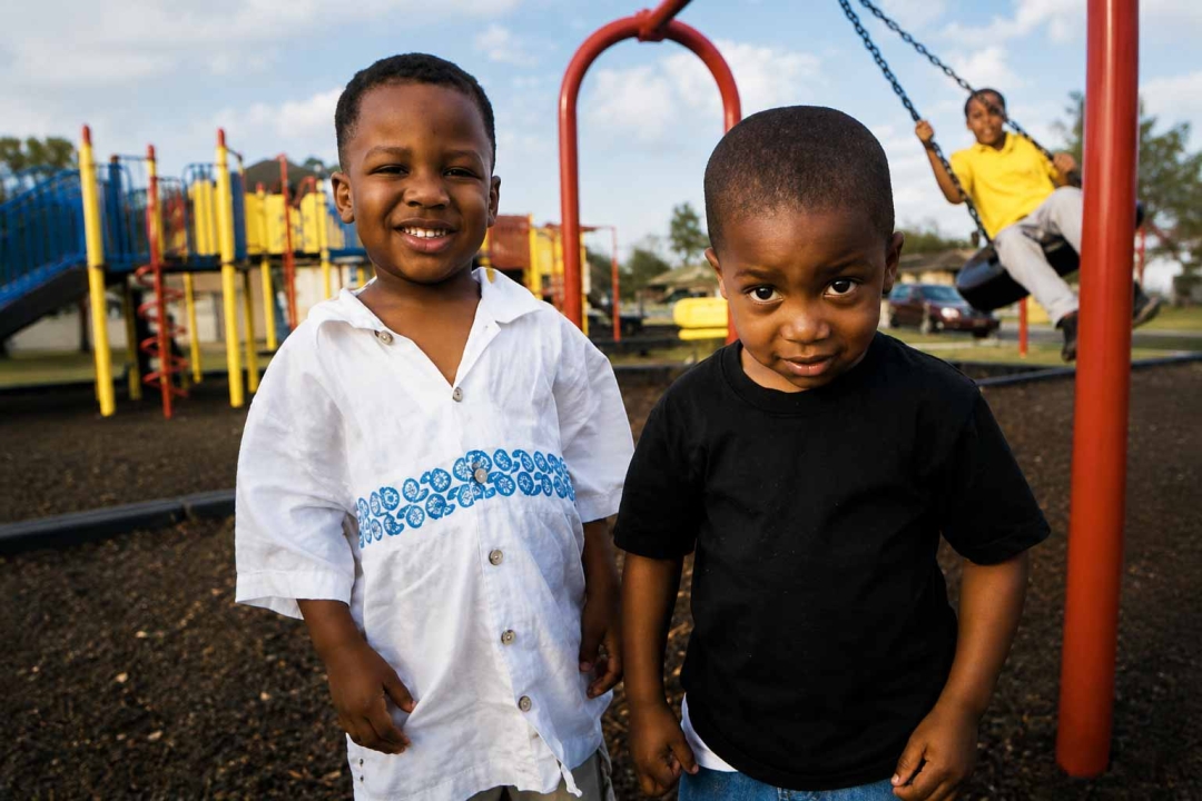 Two young boys standing in front of a colorful playground at the Acre Road Complex while a third child swings in the background