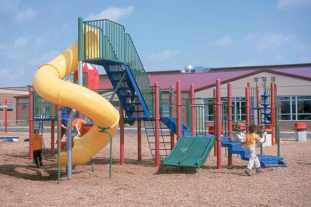 Colorful composite playground structure with a yellow spiral tube slide, ramps, and multiple play components at an elementary school