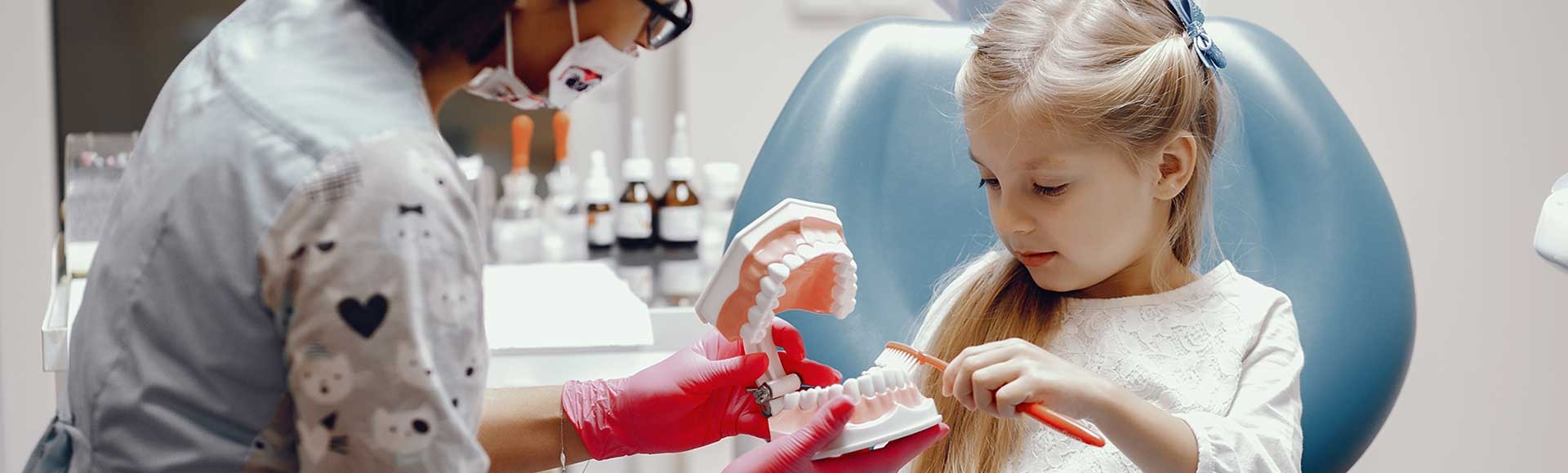 dentist teaching little girl to brush teeth