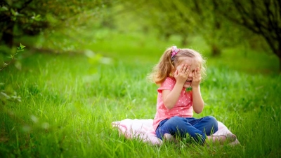Young girl playing hid in seek in green grass