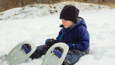 boy in snowshoes sitting in snow